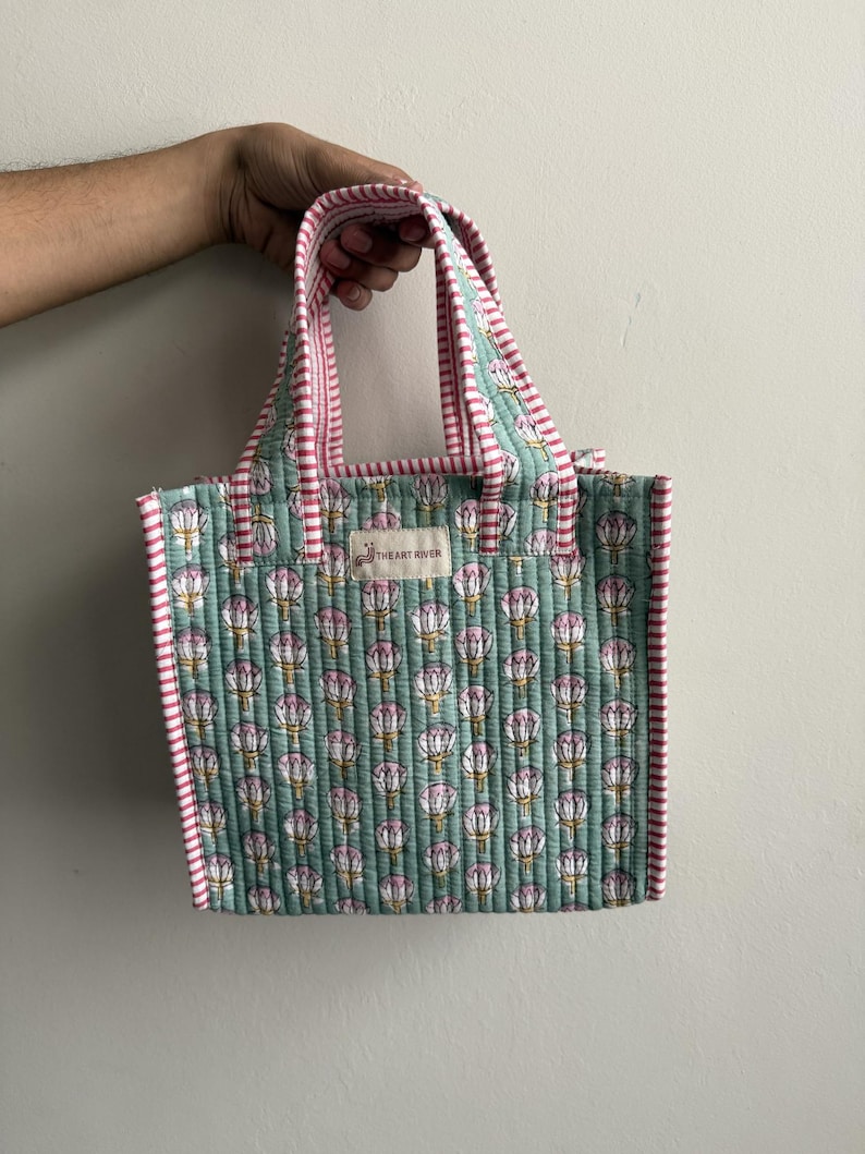 Handmade quilted cotton mini tote bag in mint green with lotus flower print, striped pink handles, and soft quilted structure for stylish everyday use.