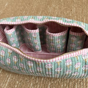 Sage green quilted cotton Dyson travel case featuring four padded compartments, pink striped lining, and spacious interior for Dyson Airwrap accessories.