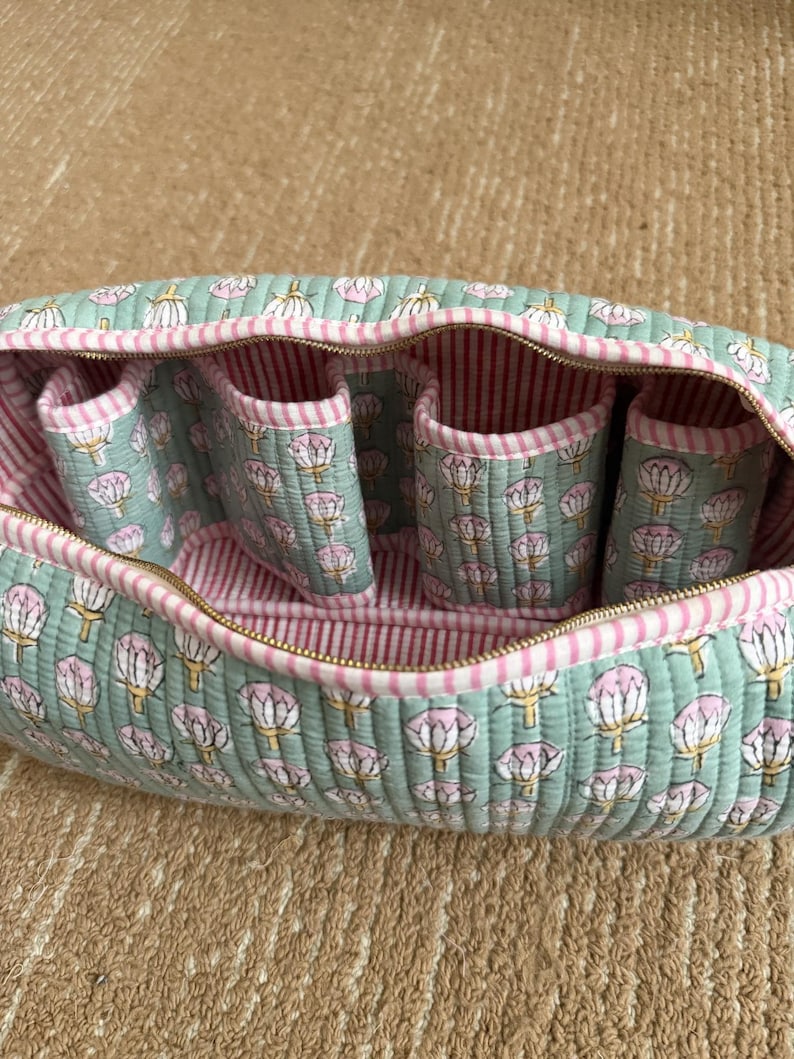 Sage green quilted cotton Dyson travel case featuring four padded compartments, pink striped lining, and spacious interior for Dyson Airwrap accessories.
