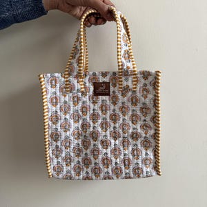 White and mustard hand block printed quilted mini lunch tote bag with striped piping and cotton handles.