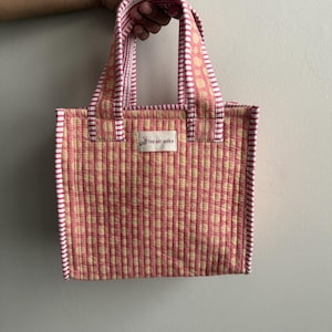Handmade quilted cotton mini tote bag in blush pink with cream polka dot print, striped pink handles, and padded construction, perfect for lunch, gifting, and everyday essentials.