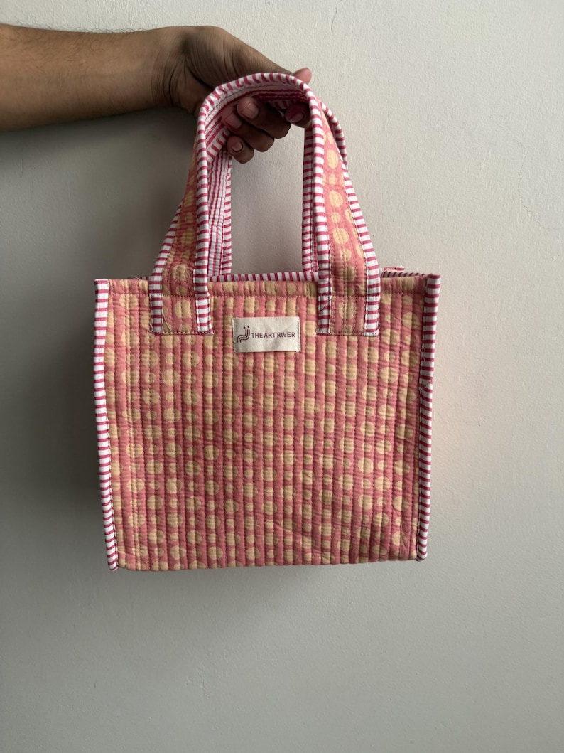 Handmade quilted cotton mini tote bag in blush pink with cream polka dot print, striped pink handles, and padded construction, perfect for lunch, gifting, and everyday essentials.