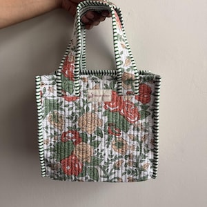 Handmade quilted cotton mini tote bag with vintage rose floral print in coral, beige, and green tones, finished with striped green handles and piping.
