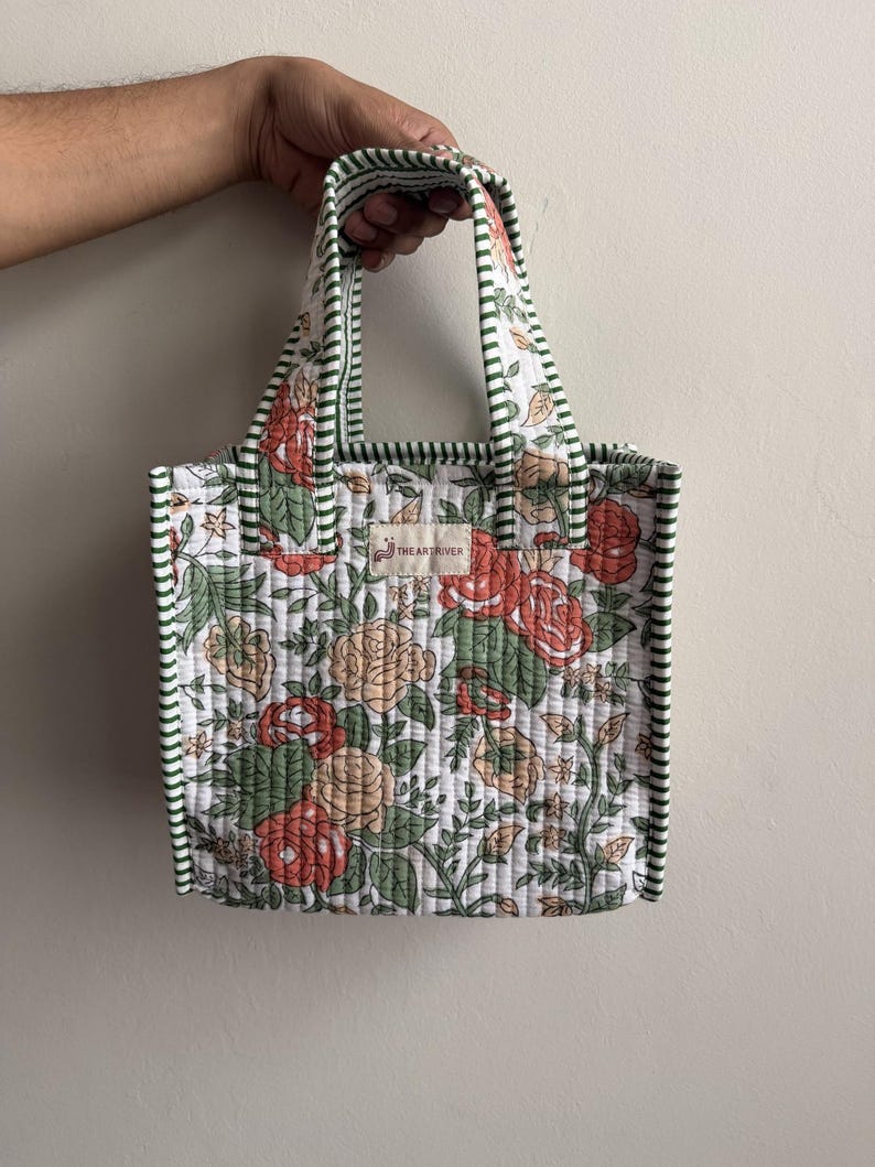 Handmade quilted cotton mini tote bag with vintage rose floral print in coral, beige, and green tones, finished with striped green handles and piping.