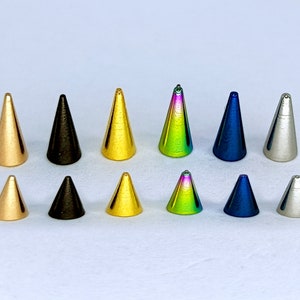 May include: A set of ten cone-shaped metal studs in various colors, including gold, silver, black, blue, and rainbow.
