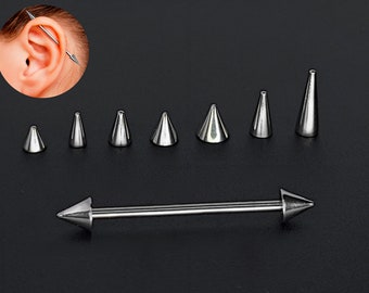 Puede incluir: Un conjunto de joyas para el cuerpo de color plateado con una variedad de extremos puntiagudos. Las joyas están dispuestas en una fila sobre una superficie gris. Las joyas incluyen una barra con extremos puntiagudos y varios extremos pequeños y puntiagudos.