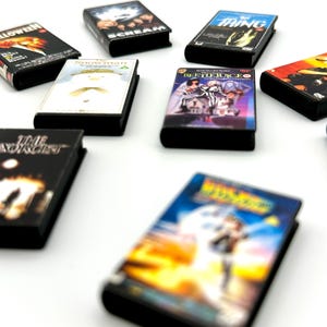 Puede incluir: Una colecci&oacute;n de mini estuches de DVD con t&iacute;tulos de pel&iacute;culas cl&aacute;sicas de terror y ciencia ficci&oacute;n. Los estuches tienen lomos negros y coloridas portadas, incluyendo "Halloween", "Scream" y "The Thing". Los DVD est&aacute;n dispuestos sobre una superficie blanca.