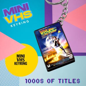 May include: Mini VHS keyring featuring the film "Back to the Future." The keyring has a silver chain and a small, rectangular case with the movie's cover art. The background includes text that says "Mini VHS Keyring" and "1000s of Titles."