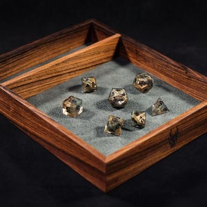 May include: A wooden dice tray with a grey felt lining. The tray has a divider and is filled with seven multi-coloured dice.