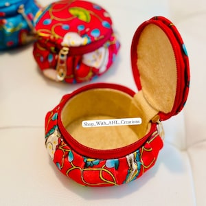 May include: A red fabric round trinket box with a zipper closure and a floral pattern. The box is open and the inside is lined with a beige fabric. The text "Shop_With_AHL_Creations" is visible inside the box.