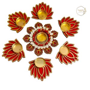 May include: A set of seven red and gold lotus-shaped diya holders with a central diya holder decorated with white seashells. The diya holders are made of wood and have a traditional Indian design.