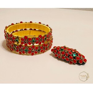 May include: Set of three gold bangles with red and green floral designs. The bangles are made of silk thread and have a traditional Indian style.