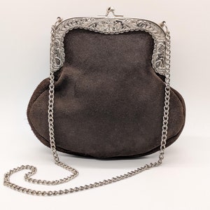 May include: A brown suede purse with a silver chain strap and a silver clasp with ornate detailing.