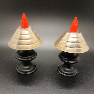 May include: A pair of vintage salt and pepper shakers shaped like lamps with black bases and silver-colored lampshades. The tops of the shakers are red and shaped like flames.