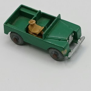 May include: A vintage green toy car with a tan driver figure. The toy car has a silver front grill and gray wheels. The open-top vehicle is a classic toy car.