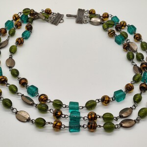 May include: A three-strand necklace with green, brown, and silver beads. The necklace has a silver clasp.