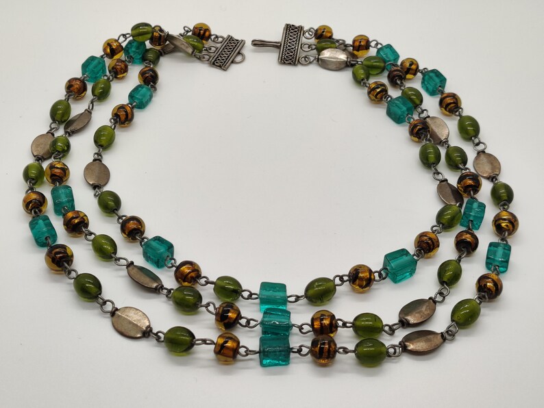 May include: A three-strand necklace with green, brown, and silver beads. The necklace has a silver clasp.