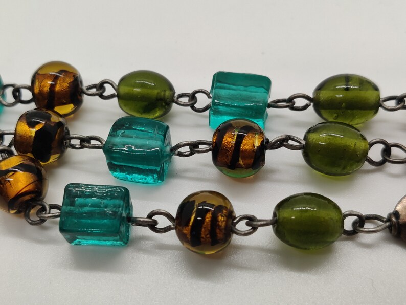 May include: A multi-colored glass bead necklace with a silver chain. The beads are green, blue, and brown.