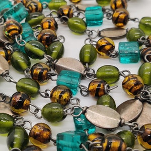 May include: A long necklace with green, brown, and turquoise glass beads. The beads are strung on a silver chain.