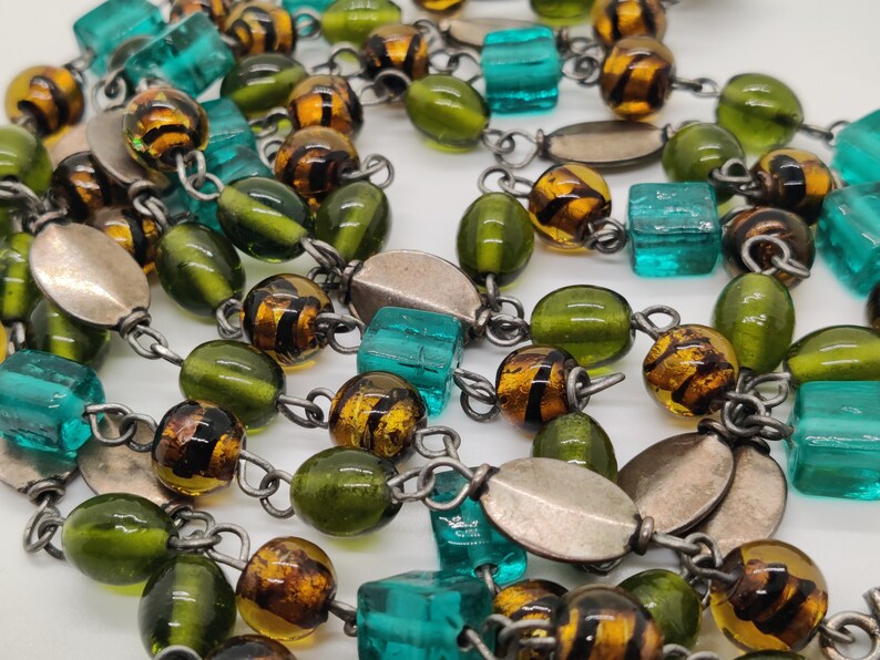 May include: A long necklace with green, brown, and turquoise glass beads. The beads are strung on a silver chain.