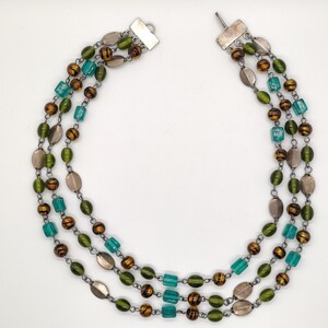 May include: A multi-strand necklace with green, brown, and silver beads. The necklace has a silver clasp.