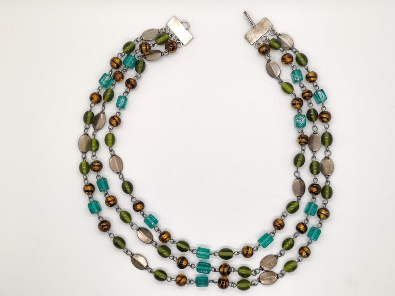 May include: A multi-strand necklace with green, brown, and silver beads. The necklace has a silver clasp.