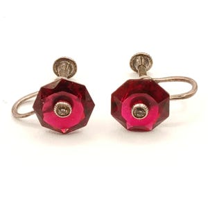 May include: A pair of vintage screw-back earrings. Each earring features a faceted, octagonal, deep red gemstone with a smaller, circular, pink center. The earrings have a silver-toned metal setting and screw mechanism.
