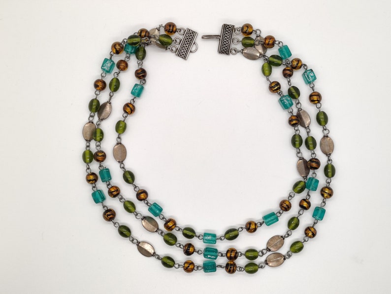 May include: A three-strand necklace with green, brown, and silver beads. The necklace has a silver clasp.