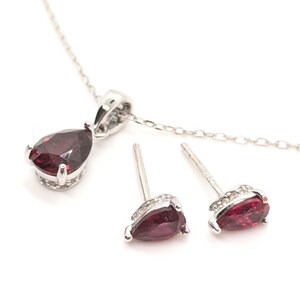 May include: A silver necklace and earrings set with pear-shaped red gemstones and small clear stones.