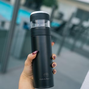 May include: A black stainless steel water bottle with a silver lid and a logo that says "Rich & Pour Co."