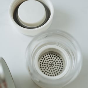 May include: A white lid with a smaller white lid inside, and a clear glass lid with a metal mesh filter inside.