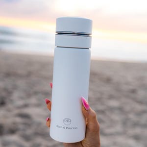 May include: White stainless steel water bottle with a silver lid and a logo that says "Rich & Pour Co."