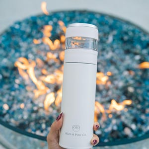 May include: White stainless steel travel mug with a clear lid and a logo that says "Rich & Pour Co."