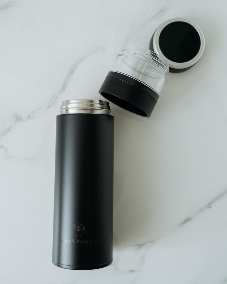 May include: A black stainless steel travel mug with a silver lid and a logo that says "Stitch & Pour Co."