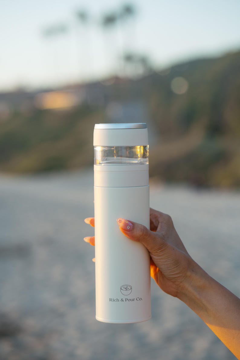 May include: White insulated travel mug with a clear lid and a silver band around the top. The mug has a logo that says "Rich & Pour Co."