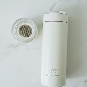 May include: White stainless steel travel mug with a lid and a logo that says "Rich & Pour Co."