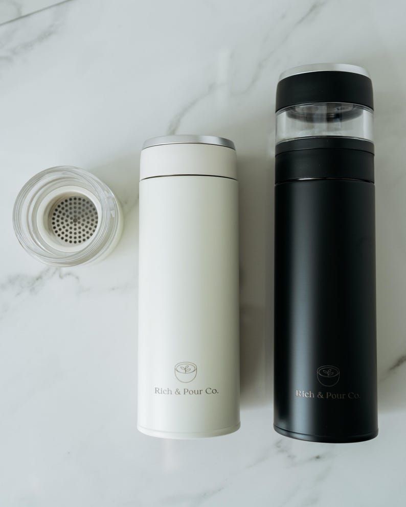 May include: Two stainless steel thermal coffee tumblers with a built-in infuser. The tumbler on the left is white with the text "Rich & Pour Co." The tumbler on the right is black with the text "Rich & Pour Co."