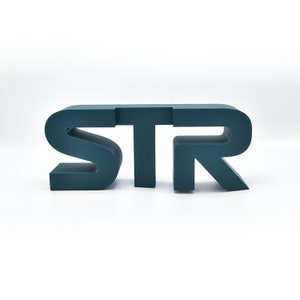 Puede incluir: Un letrero impreso en 3D de color azul verdoso que dice "STR".