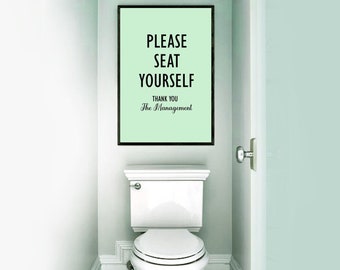 May include: A framed sign with the text "PLEASE SEAT YOURSELF" and "THANK YOU The Management" hangs above a white toilet. The sign has a light green background and a black frame. The bathroom walls are light green.