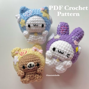 Könnte beinhalten: Drei gehäkelte Stofftiere: ein weißes Kaninchen mit einem blau-weißen Sternenhut, ein lila Kaninchen mit einem lila-weißen Sternenhut und ein brauner Bär mit einem gelb-weißen Sternenhut.  PDF Häkelanleitung.