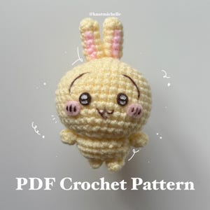 Könnte beinhalten: Ein gehäkeltes Spielzeugkaninchen in Hellgelb mit rosa Akzenten an Ohren und Wangen. Das Kaninchen hat schwarze Augen und ein lächelndes Gesicht. Der Text "PDF Crochet Pattern" ist unten zu sehen.