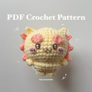 Könnte beinhalten: Ein handgefertigtes Häkeltier in Form einer Cartoonfigur mit gelbem Körper, rosa Akzenten und schwarzen Augen. Der Text "PDF Crochet Pattern" steht oben. Das Spielzeug hat ein lächelndes Gesicht. Der Handle des Erstellers, @knotmichelle, steht unten.