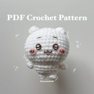 Könnte beinhalten: Ein weißer Häkelbär mit rosa Wangen, braunen Augen und einer kleinen braunen Nase. Der Bär hat kleine Arme und Beine. Der Text auf dem Bild lautet "PDF Crochet Pattern" und "@knotmichelle".