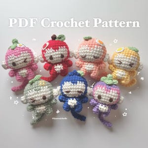 May include: A collection of seven small, colorful crocheted monkey dolls, each featuring a unique fruit-themed hat, a cream-colored face, and a long tail. The text PDF Crochet Pattern is displayed at the top, with small white star and hash symbols.