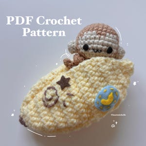 May include: A handmade crochet monkey toy in a yellow banana-shaped bed, with a brown star and a blue and yellow moon decoration. The image includes the text "PDF Crochet Pattern".