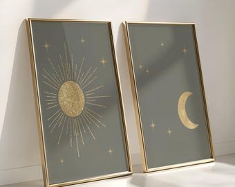 May include: Two framed art prints featuring celestial designs. One print displays a gold sunburst, the other a gold crescent moon, both against a muted green background. Gold stars are scattered across the backgrounds. The frames are gold.