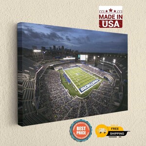 May include: A rectangular canvas wall art print featuring an aerial night view of a football stadium with a green field, bright stadium lights, and a city skyline in the background. The word PANTHERS is printed in large white letters on the field.