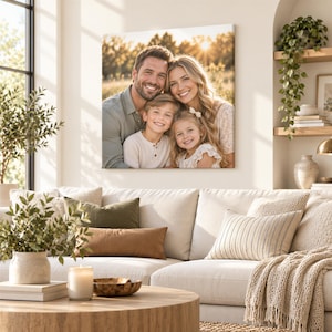 A family portrait of a man, woman, and two children is displayed on the wall above a beige sofa in a cozy living room setting.