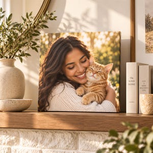 A framed photograph of a woman embracing a cat is displayed on a wooden shelf, surrounded by decorative items such as a vase with greenery and books.