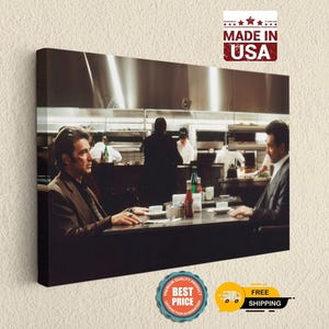 May include: A rectangular canvas wall art print featuring a scene from the movie Heat with two individuals sitting at a restaurant table. The image shows a dimly lit interior with a stainless steel kitchen background and a red ketchup bottle.